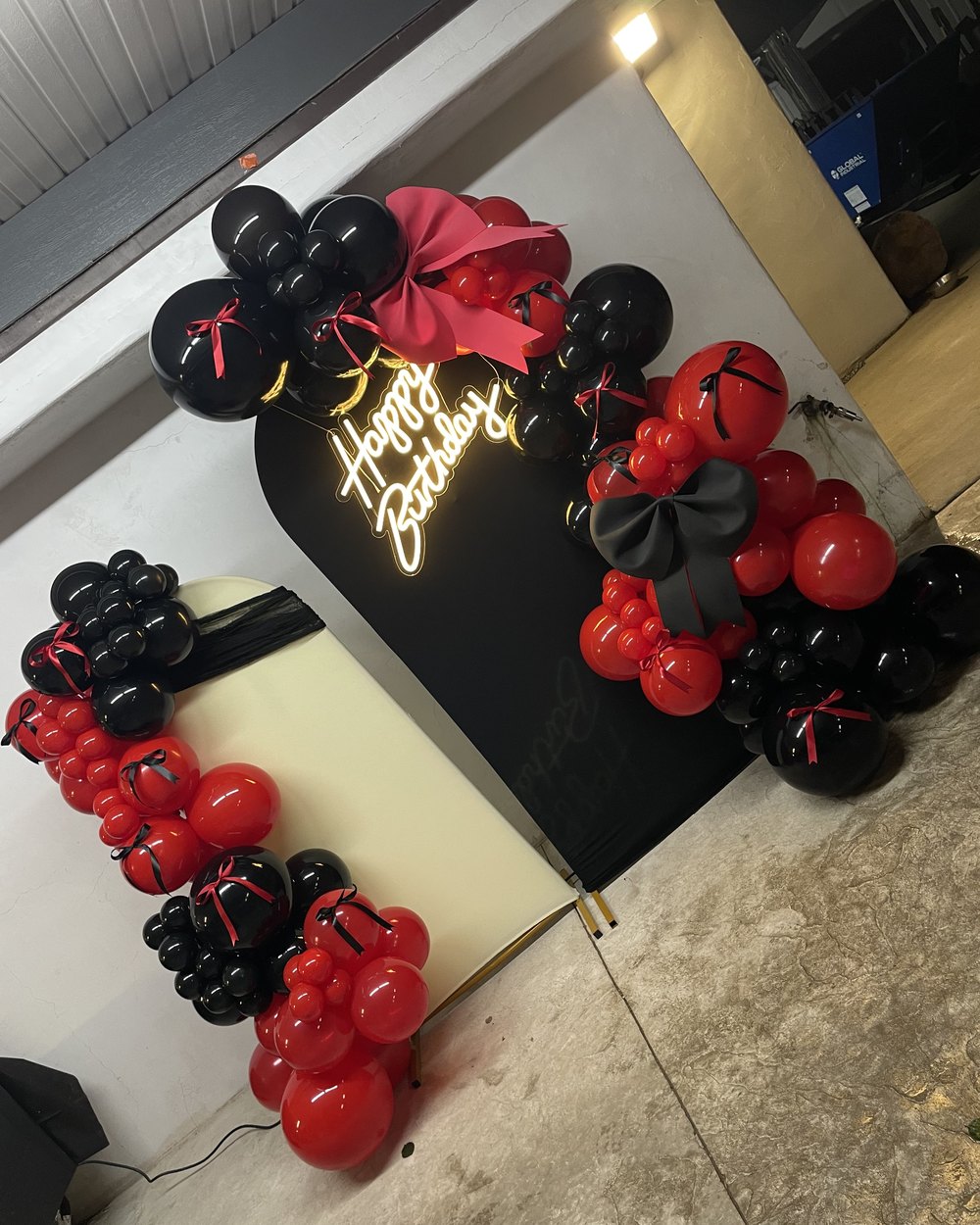 A black backdrop with a neon Happy Birthday sign and red and black balloon garlands