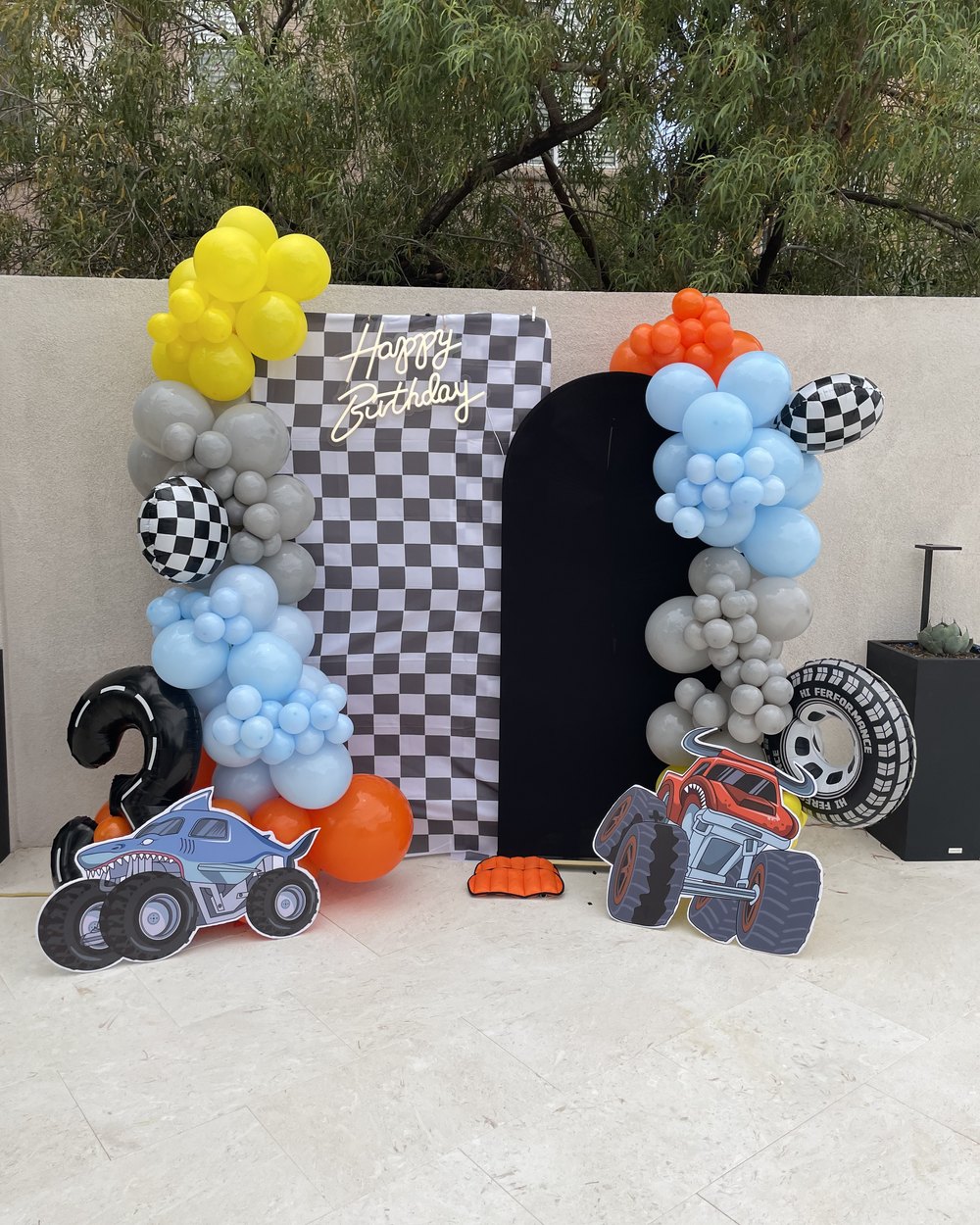 Monster truck themed setup with a checkered backdrop and blue, grey and orange balloons