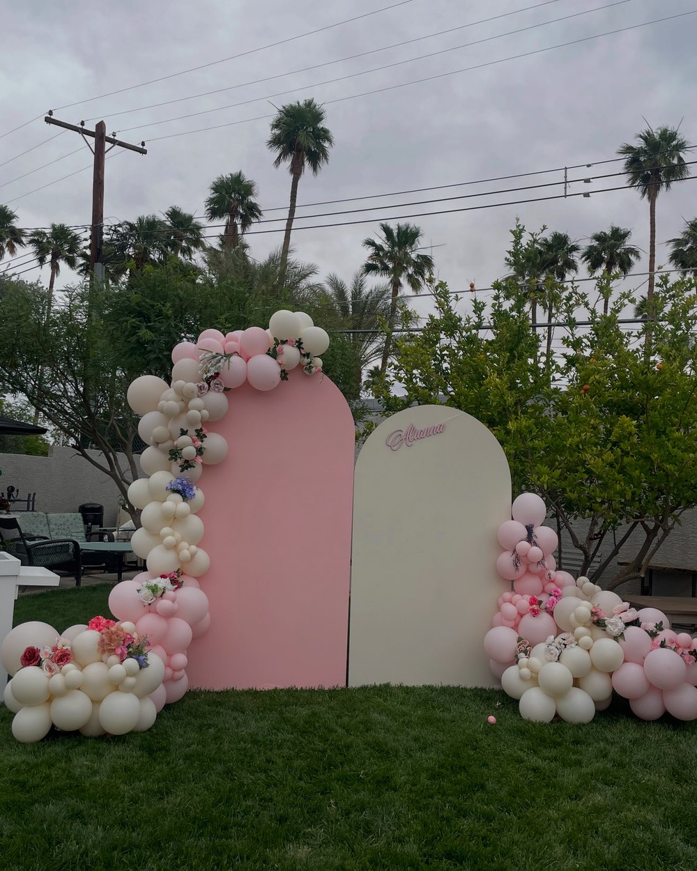 Pink and cream arched panels with cream and pink balloon garlands and flowers, on a lawn