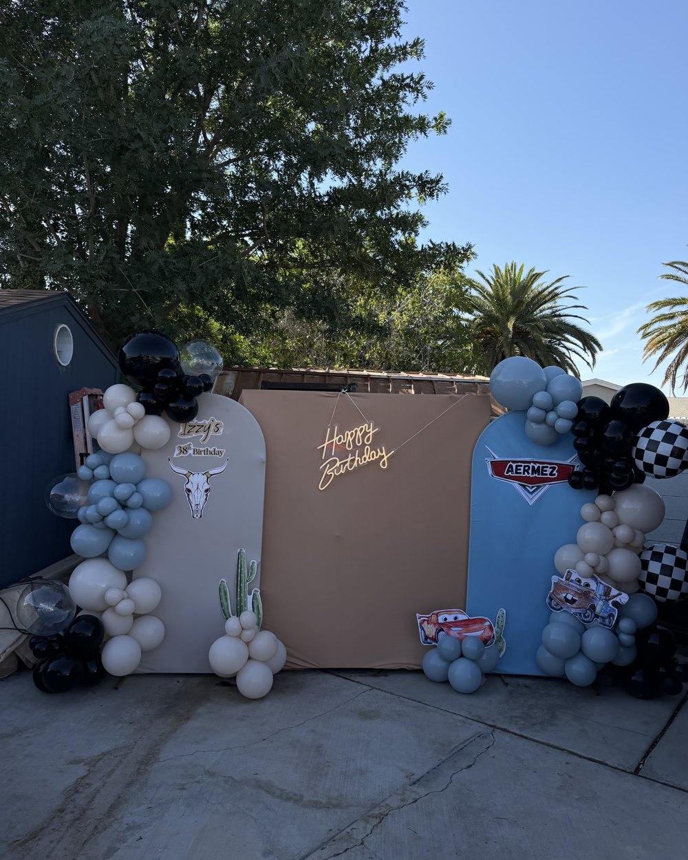 Three panels in cream, tan and blue with printed cutouts, a neon sign and blue, black and cream balloons
