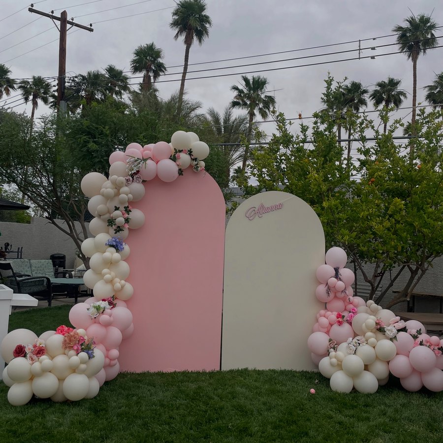 Two arched panels in pink and cream with cream and pink balloon garlands, set up on a lawn