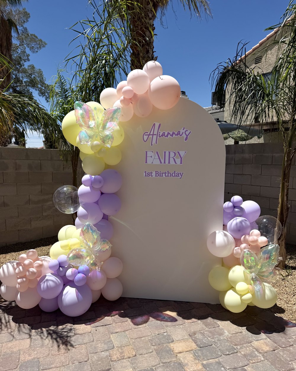 A single arched backdrop for a fairy first birthday with lavender, yellow and pink balloons